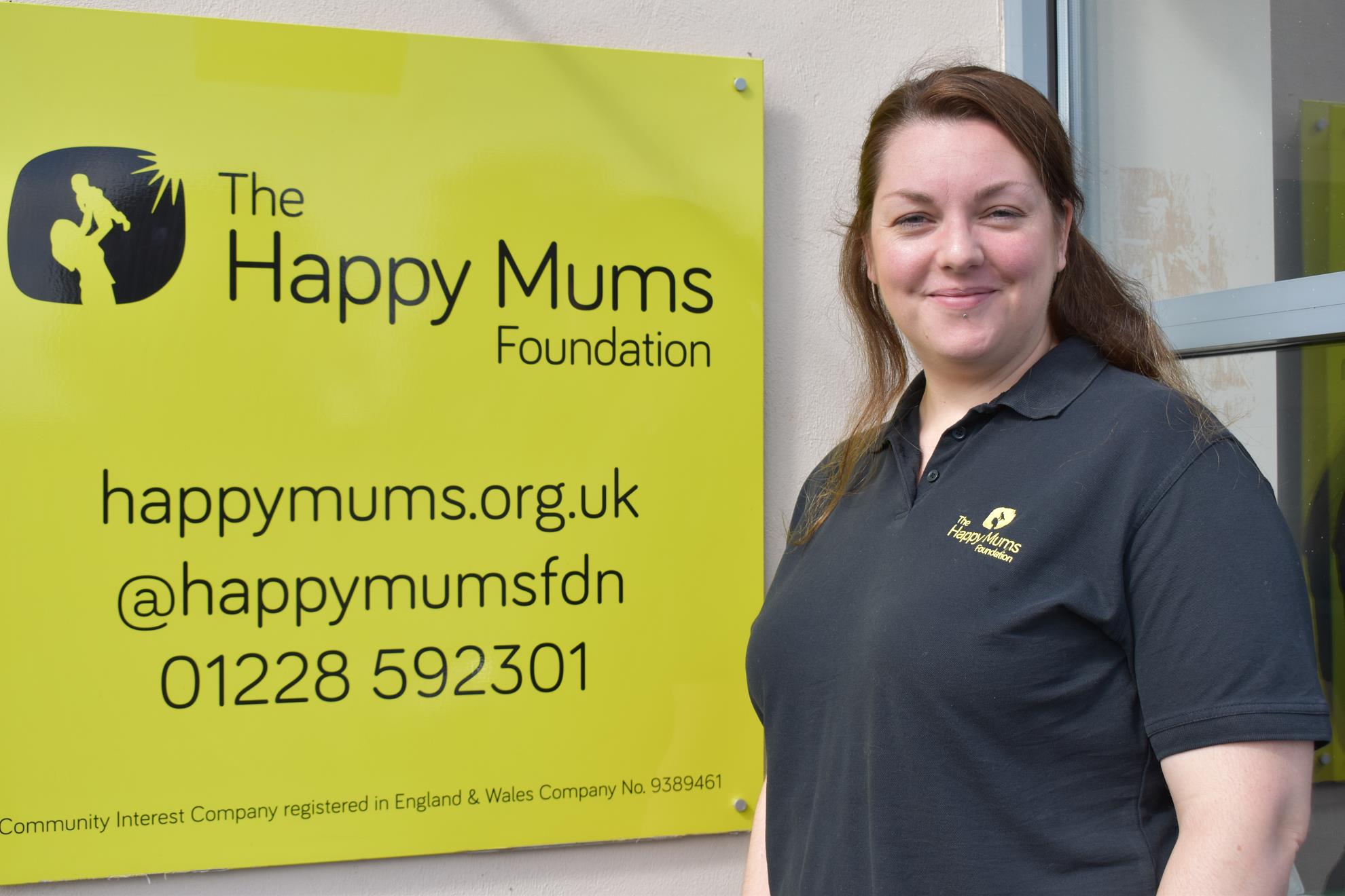 Katherine Dalgliesh, Founder of Happy Mums, standing next to a yellow sign with the happy mums logo and contact details on