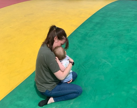 A Mum kneeling and hugging her baby close, both looking away from the camera 