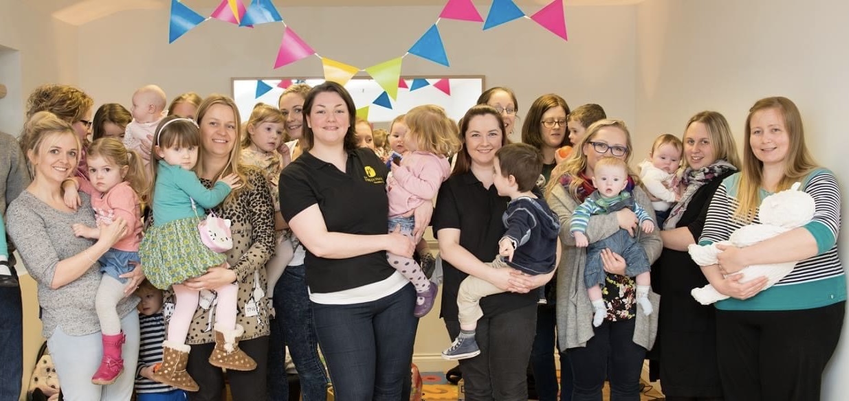 Katherine Dalgleish and Gemma Cairns surrounded by Mums and little ones under colourful bunting